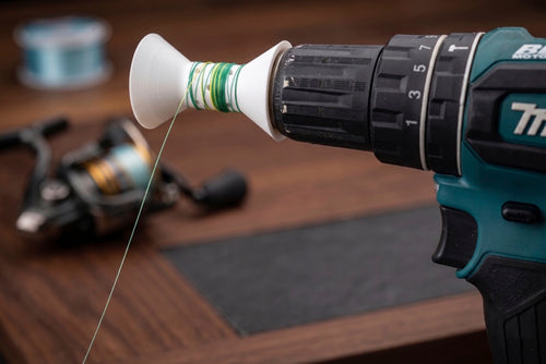 Drill being used to unwind fishing line from a spool on a wooden surface.